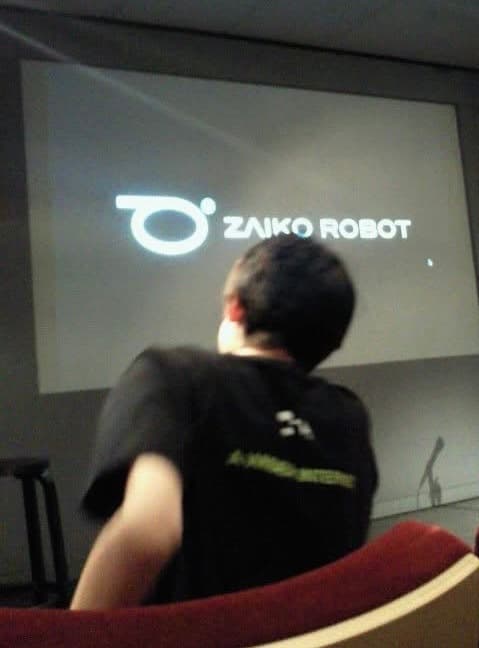 ZAIKO ROBOTのロゴが映るスクリーンを見つめる人物